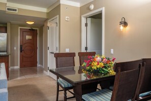 A dining area with a glass table, cushioned chairs, a floral centerpiece, and a wall-mounted light fixture.