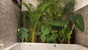 A modern bathroom with a freestanding bathtub, surrounded by lush green plants and a wooden floor. - Casa de campo cerca al aeropuerto MDE (Rionegro)