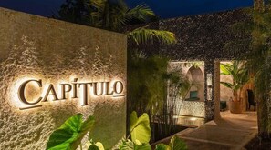 A stone wall with the name 'Capitulo' illuminated, a pathway leading to a building entrance, and tropical plants. - Casa de campo cerca al aeropuerto MDE (Rionegro)