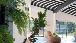 A modern interior with a wooden bench, large windows, and indoor plants. - Casa de campo cerca al aeropuerto MDE (Rionegro)