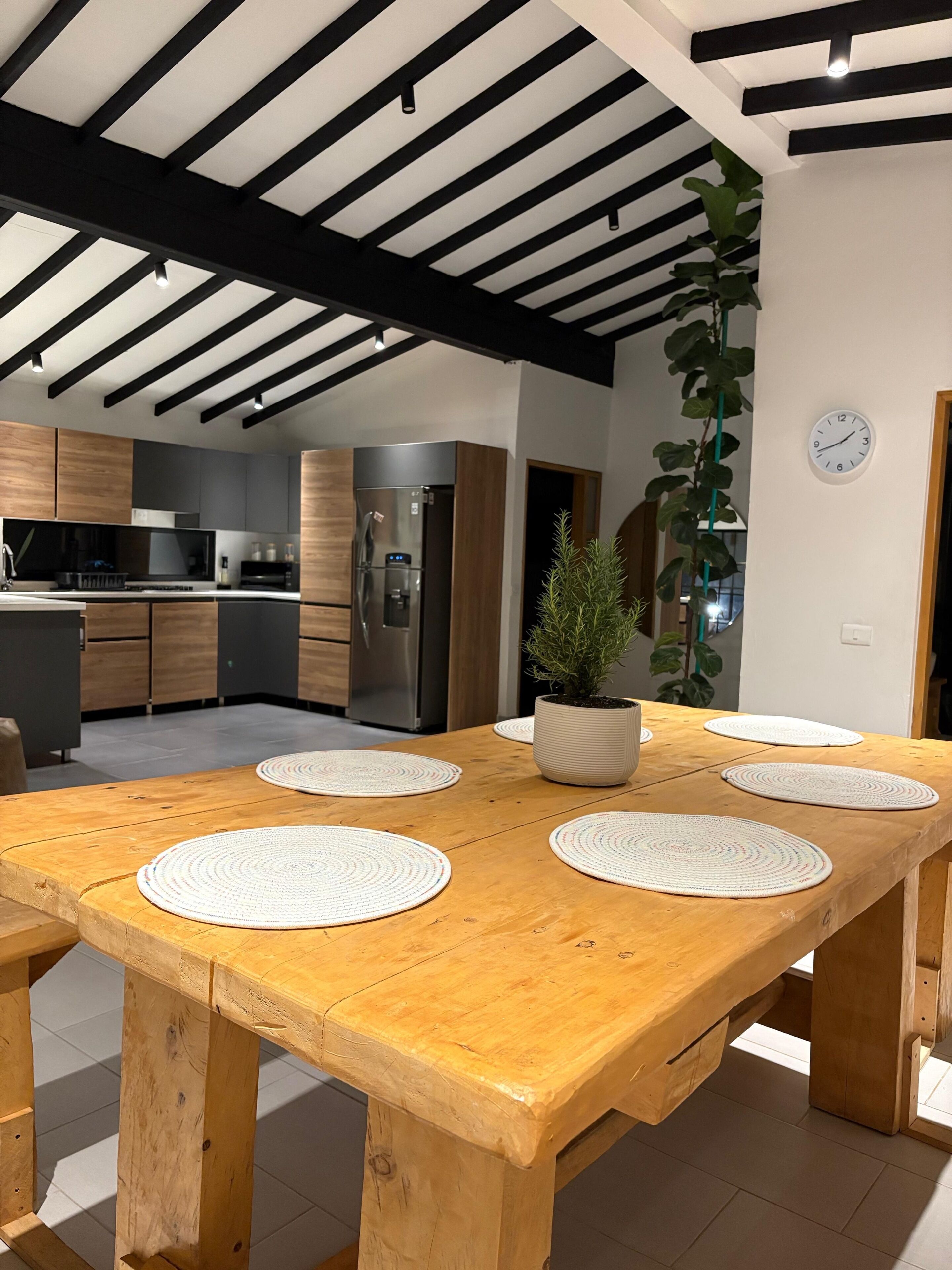 Een moderne keuken met houten kasten, een roestvrijstalen koelkast en een eethoek met een houten tafel en vier placemats.
