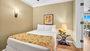 Camera d'albergo con un letto, una lampada a muro, un quadro incorniciato, un comodino con lampada e una ventola a soffitto.