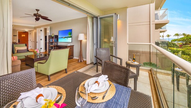 Un balcone d'hotel con un tavolo da pranzo apparecchiato, un divano e una TV sullo sfondo.