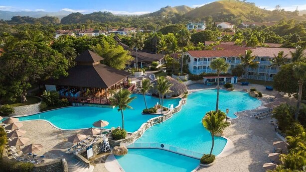 Et resort med flere swimmingpools, palmer og et bjergrigt baggrundsmotiv.
