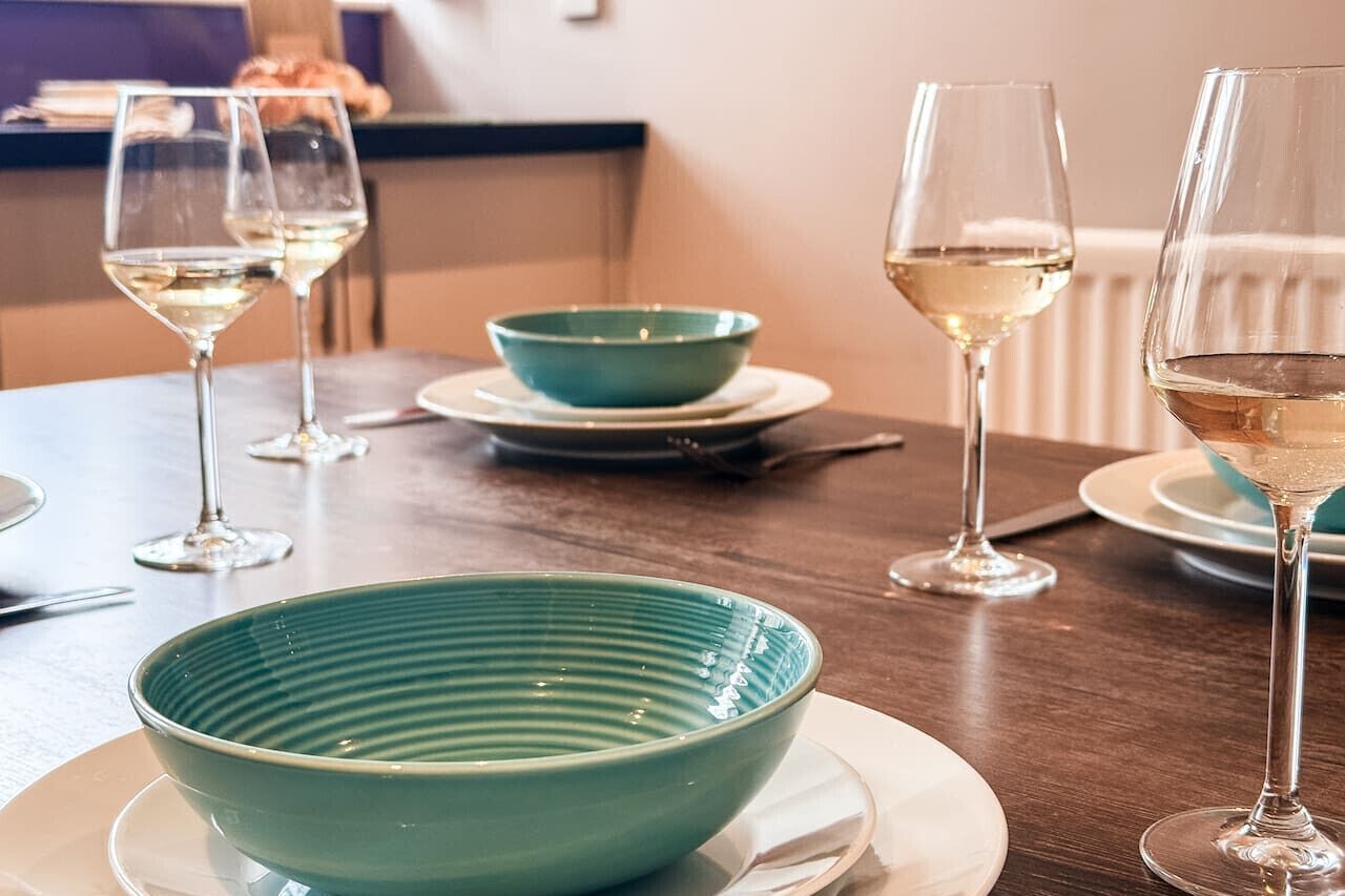 A dining table with a teal bowl, wine glasses, and plates.
