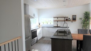 Eine moderne Küche mit Edelstahlkühlschrank, Backofen und Spüle, Holzboden und einem Fenster mit Blick auf Grünflächen.