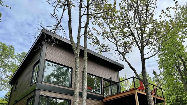 Ein modernes, zweistöckiges Haus mit großen Fenstern, einem Balkon und einer Holzterrasse.