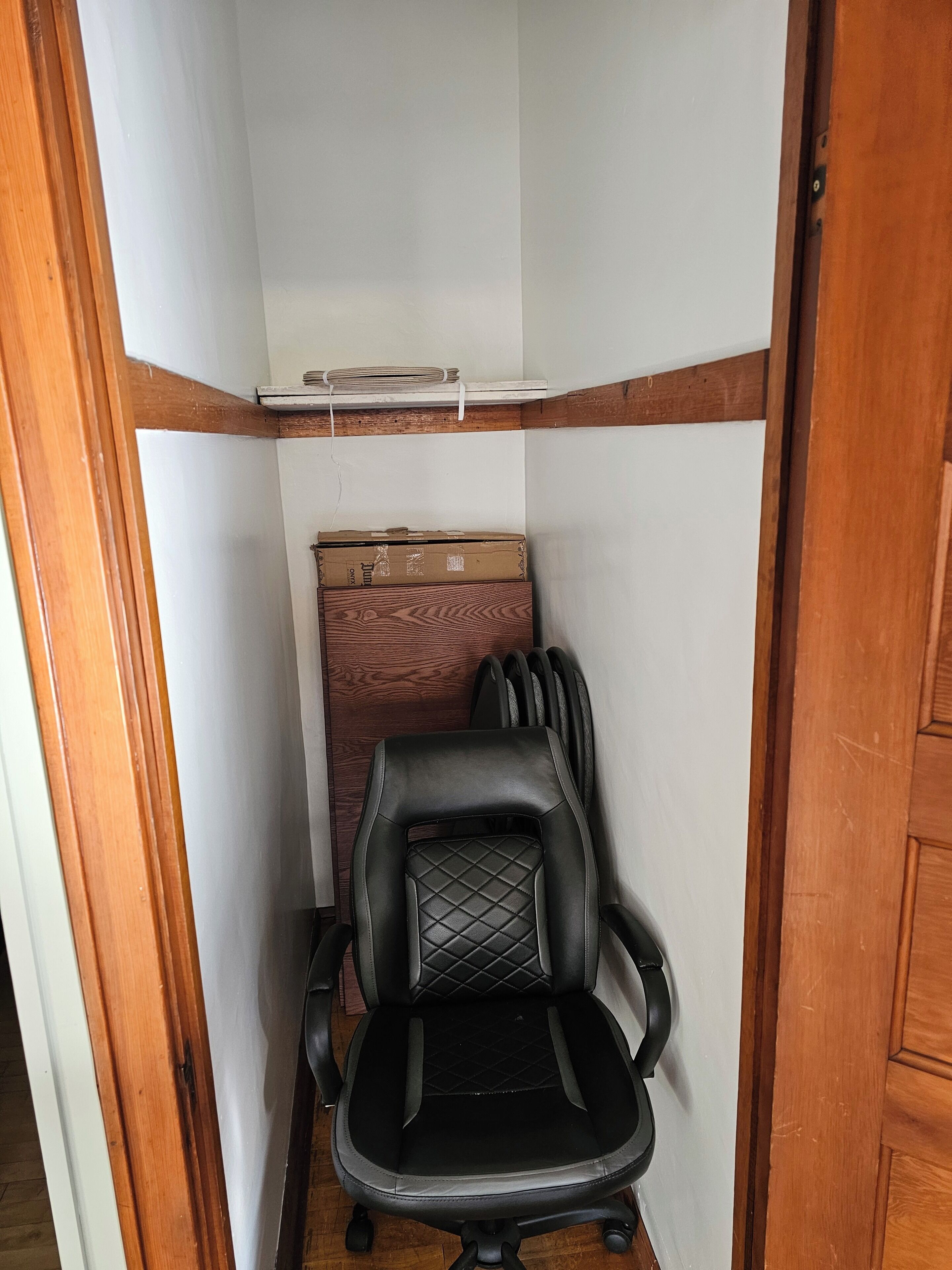 Une pièce étroite avec une porte à cadre en bois, un fauteuil de bureau noir et un meuble en bois adossé au mur.