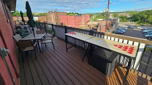 A wooden deck with outdoor seating, a ping pong table, and a view of a parking lot and buildings.