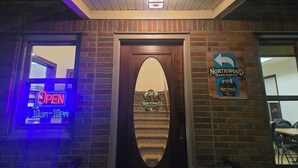 A brick building entrance with a neon 'OPEN' sign, a door with a Northwood Cafe Haven logo, and a directional sign.