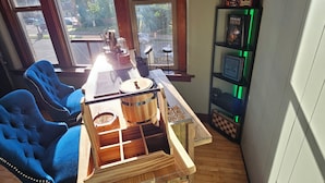 A room with a wooden table, two blue chairs, a bookshelf, and large windows.