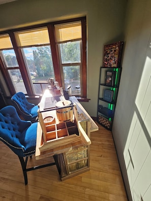 A room with a wooden table, two blue chairs, a bookshelf, and large windows.