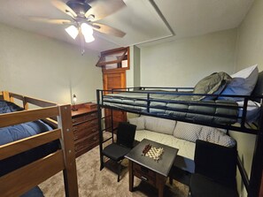 Quarto com beliche, escrivaninha, cadeira e ventilador de teto.