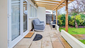 Eine überdachte Terrasse mit einer Holz-Pergola, einer gepolsterten Sitzecke und einem kleinen Tisch.