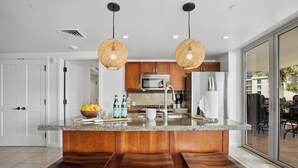 A modern kitchen with a central island, wooden bar stools, stainless steel appliances, and a view to the outside. - Honua Kai | Ocean View 4 BR, Sleeps 14 | Car Incl. w/ 6+ Nights | HKH ML-2801 by KBM (Lahaina)