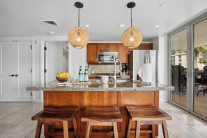 A modern kitchen with a central island, wooden bar stools, stainless steel appliances, and a view to the outside. - 3 Honua Kai Villas | Ocean View | Sleeps 16 | Free Car w/ 6+ Nights | ML-2810 (Lahaina)