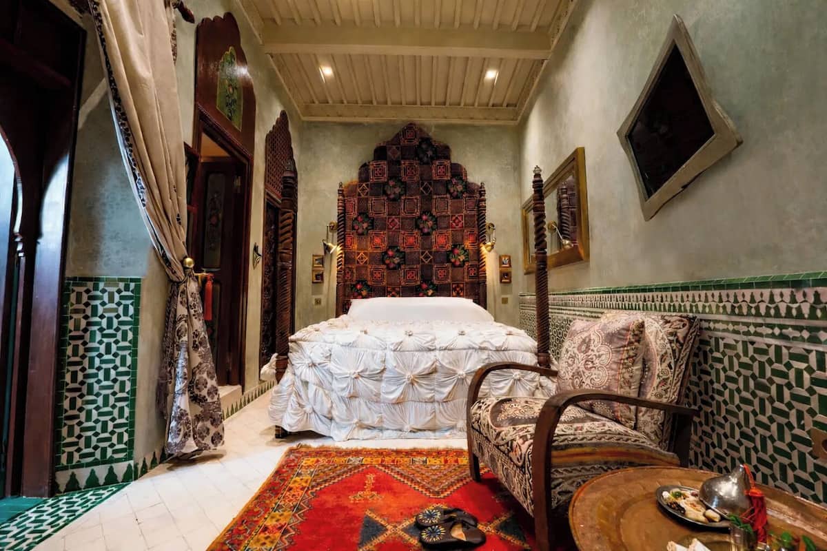 A traditional Moroccan room with a bed, a sofa, a patterned wall, and a tiled floor.