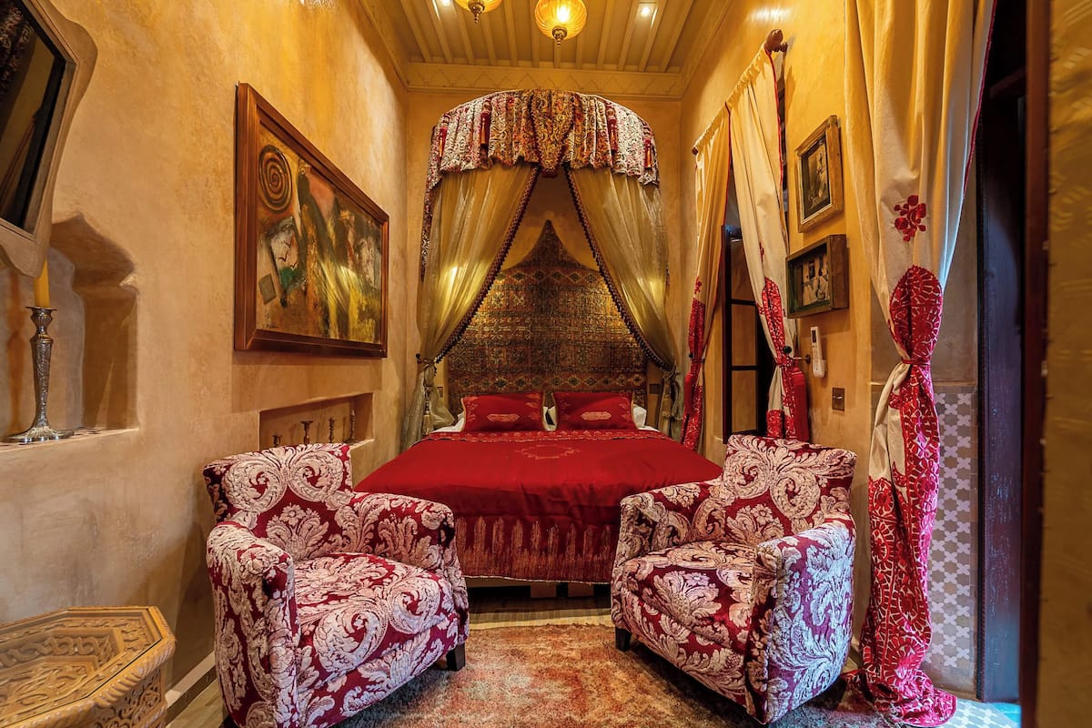 A room with a large bed, two ornate armchairs, a patterned rug, and a decorative canopy over the bed.