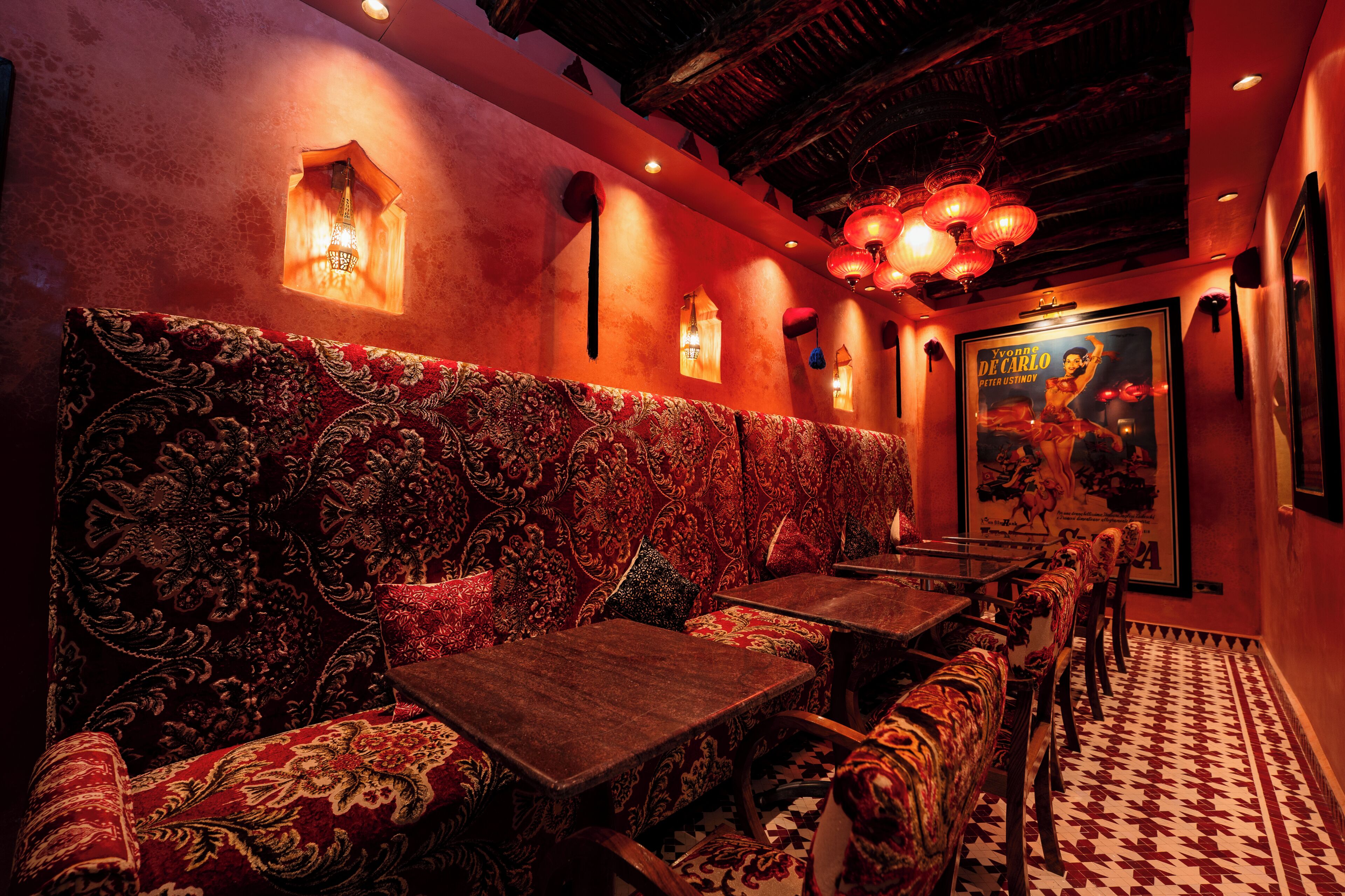 A restaurant with patterned upholstery, wooden tables, and wall-mounted lights.
