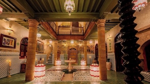 An interior with ornate columns, a central fountain, patterned flooring, and a balcony with a view.