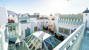 A rooftop with a glass balustrade, a small seating area, and a view of the surrounding buildings.