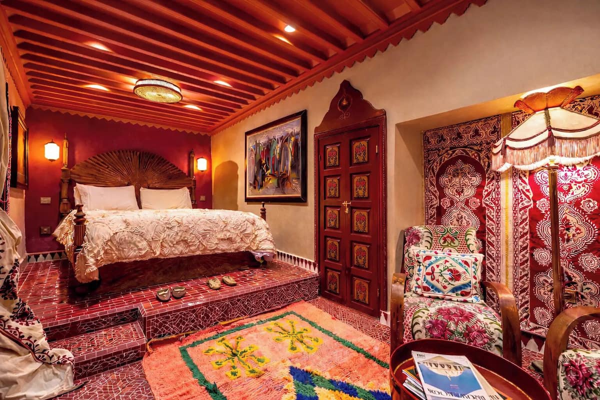 A traditional room with a bed, a patterned rug, a wooden door, and a chair with a floral design.