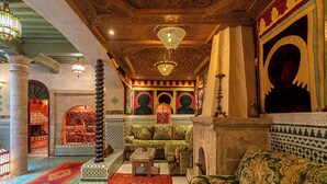 An interior with a patterned carpet, a sofa, a pillar, and a wall with a geometric design.