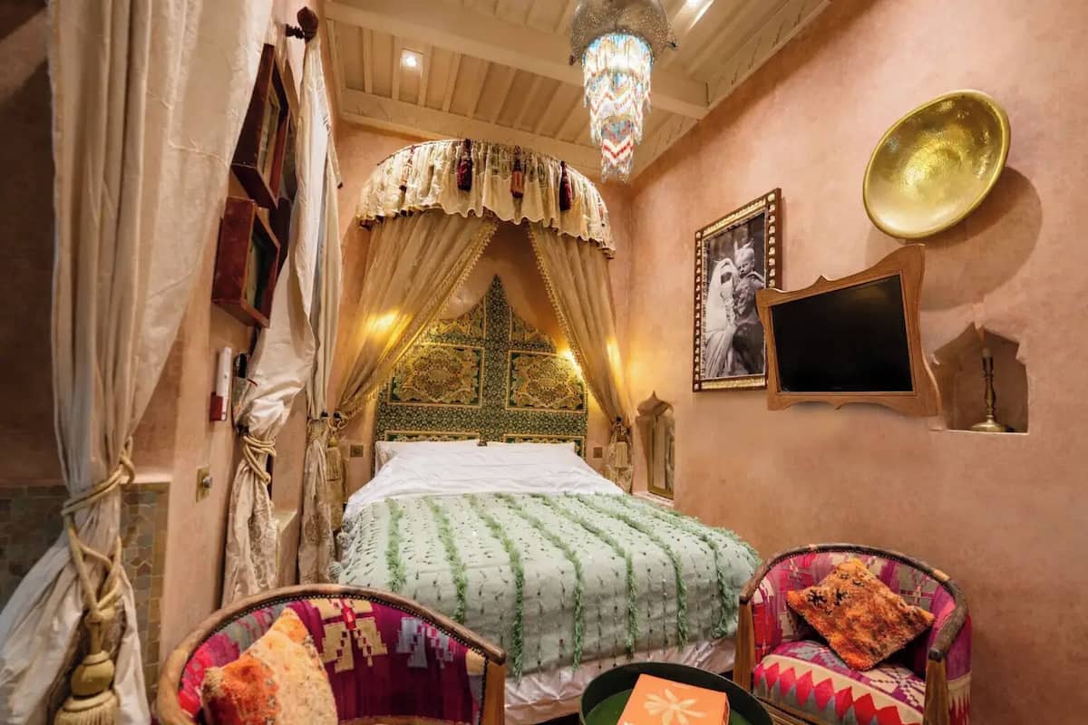 A traditional room with a bed, a chandelier, a wall-mounted television, and a decorative plate.