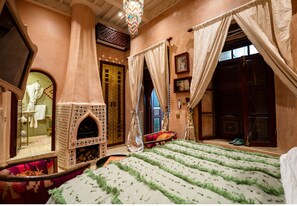 A traditional Moroccan room with a patterned rug, a decorative fireplace, and a view of the outside.