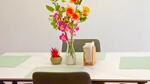 Ein Esstisch mit Blumen in einer Vase, einer kleinen Topfpflanze und einer Taschentuchbox.