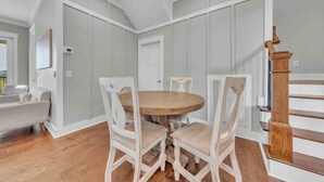 Un espace repas avec une table ronde en bois et des chaises à revêtement blanc, un escalier avec des balustrades en bois et une porte blanche.