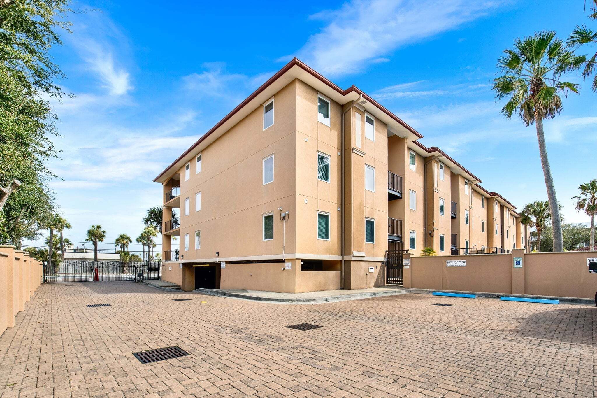 A multi-story building with a flat roof, a gated entrance, and a paved courtyard.