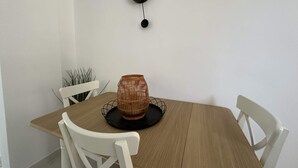 Ein Esstisch mit einer Uhr an der Wand, weißen Stühlen und einem gewebten Korb darauf.