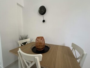 A dining table with a clock on the wall, white chairs, and a woven basket on the table. - Loutra Suites Natural Springs View (Corinth)