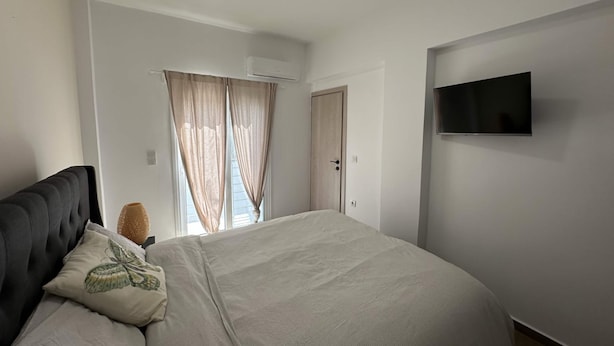 Ein Schlafzimmer mit Bett, Fernseher an der Wand und einem Fenster mit Vorhängen.