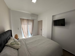 Et soveværelse med en seng, et fjernsyn på væggen og et vindue med gardiner.