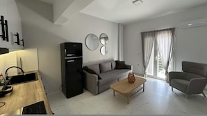 Ein modernes Wohnzimmer mit einer Couch, einem Couchtisch, einem Fernseher und einer Küchenzeile inklusive Spüle und Schränken.