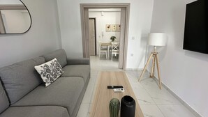 A modern living room with a grey sofa, a wooden coffee table, a cactus, a black vase, a remote control, and a lamp. - Loutra Suites Aegean Wave Suite (Corinth)