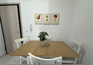Zona pranzo con tavolo in legno, sedie bianche e una pianta in vaso.