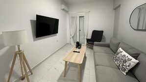 A modern living room with a flat-screen TV, a wooden coffee table, a grey sofa, a black armchair, and a small table with decorative items. - Loutra Suites Aegean Wave Suite (Corinth)