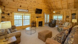A log cabin interior with a fireplace, a television, and a cozy seating area. - Mountain Paradise | Mtn View, Hot Tub + FREE Tickets (Sevierville)