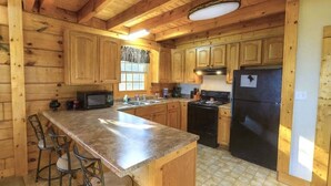 A wooden cabin kitchen with a granite countertop, wooden cabinets, a black refrigerator, and a window with blinds. - Mountain Paradise | Mtn View, Hot Tub + FREE Tickets (Sevierville)