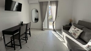 A modern living room with a flat-screen TV, a dining table, a sofa, and a large mirror. - Loutra Suites Sunlit Cove Studio (Corinth)