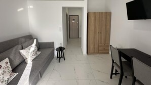 A modern living room with a sofa, a small table, a TV, and a wooden wardrobe. - Loutra Suites Sunlit Cove Studio (Corinth)