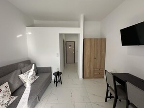 A modern living room with a sofa, a small table, a TV, and a wooden wardrobe. - Loutra Suites Sunlit Cove Studio (Corinth)