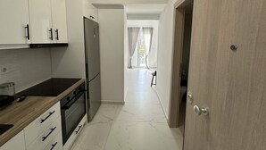 A modern kitchen with white cabinets, a black countertop, and a built-in oven. - Loutra Suites Sunlit Cove Studio (Corinth)