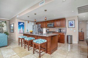 A spacious kitchen with a central island, bar stools, and a dining area with a view. - Honua Kai | Ocean View 4 BR, Sleeps 12 | Car Incl. w/ 6+ Nights | HKK ML-3158 by KBM (Lahaina)