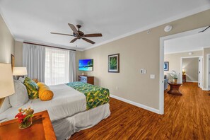 A hotel room with a bed, ceiling fan, TV, artwork, and a hallway leading to another room. - 3 Honua Kai Villas | Ocean Front | Sleeps 18 | Free Car w/ 6+ Nights | ML-3161 (Lahaina)