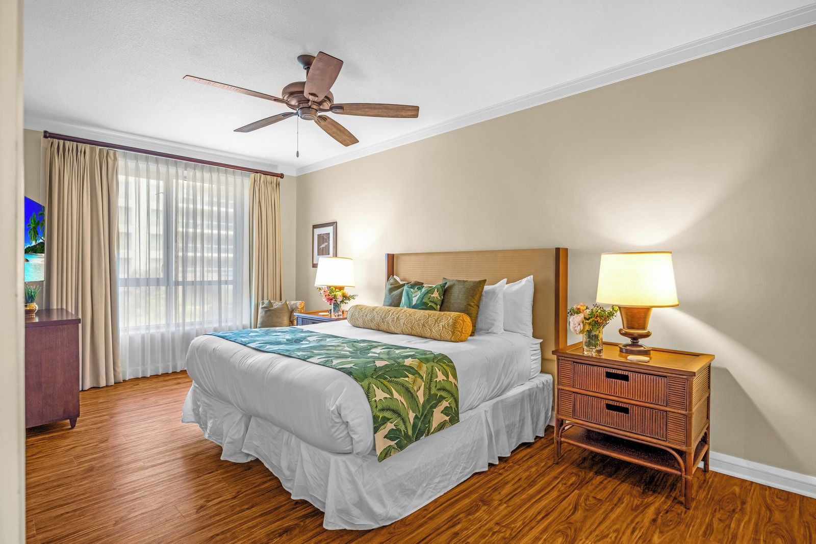 Une chambre d’hôtel avec un lit, un ventilateur de plafond, une table de chevet avec une lampe et une vue sur l’extérieur par la fenêtre.