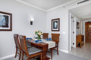 A dining area with a table set for four, chairs, a vase with flowers, and framed artwork on the walls. - 4 Honua Kai Villas | Ocean Front | Sleeps 24 | Free Car w/ 6+ Nights | ML-3164 (Lahaina)